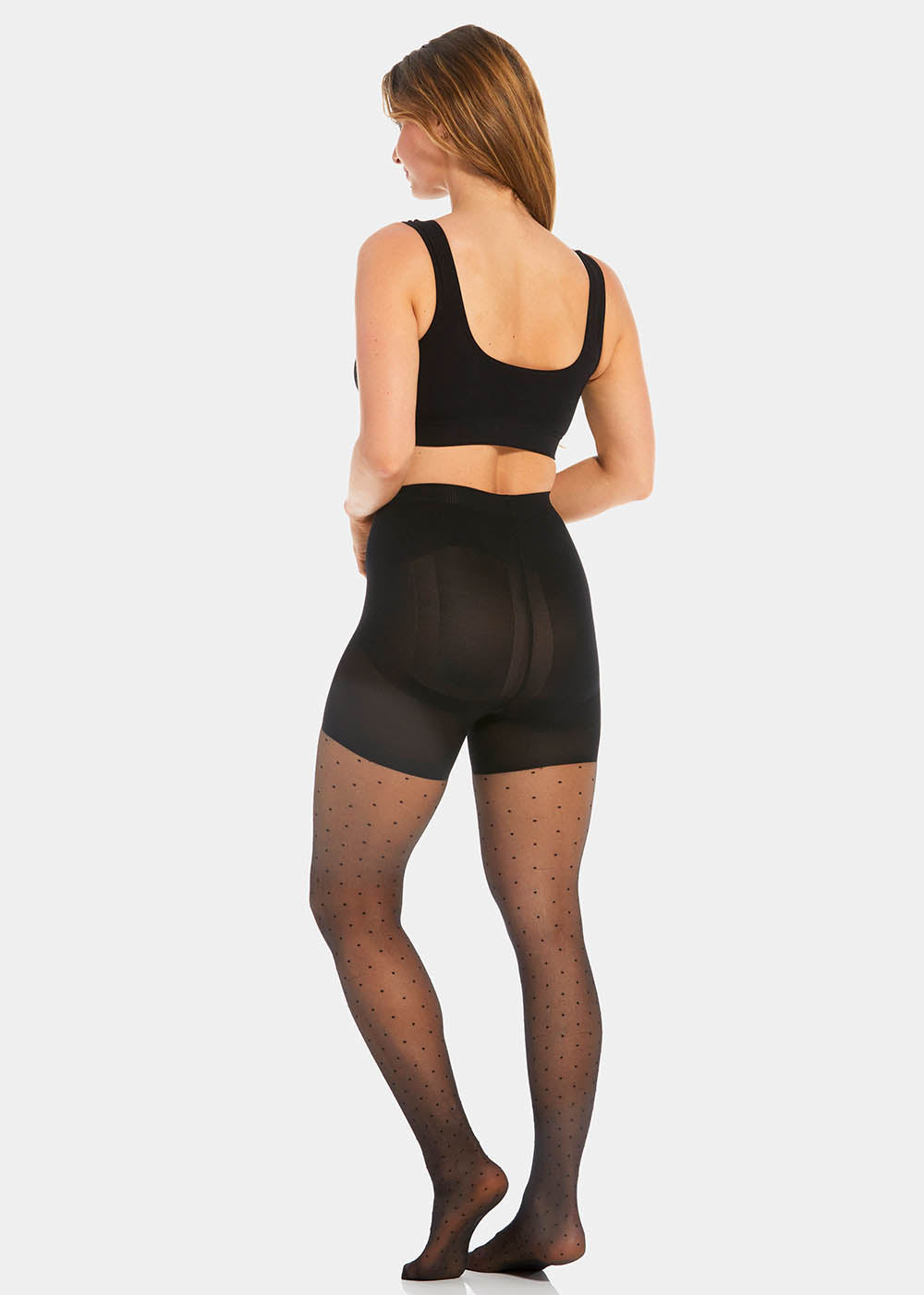 Back view of a model wearing Sexy Dots shaping tights in black, 20 denier sheer tights with dot pattern. Built-in firm shaping shorts providing control for lower back, hips, and upper legs, with subtle lift at the bottom and reinforced toes visible.