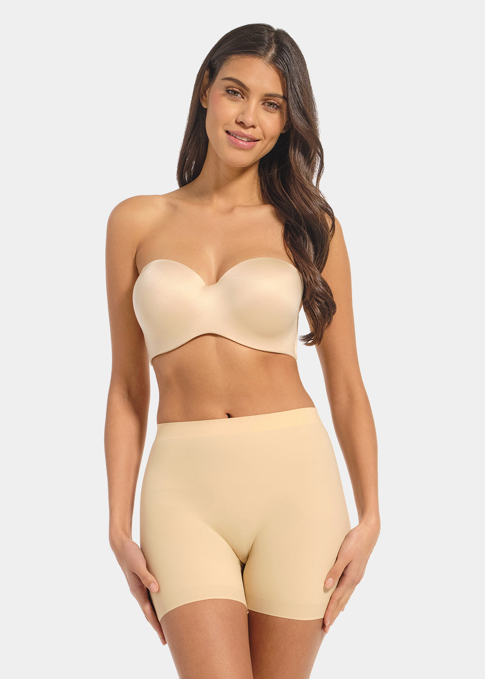 Woman wearing a beige strapless top and high-waisted shorts on a light gray background