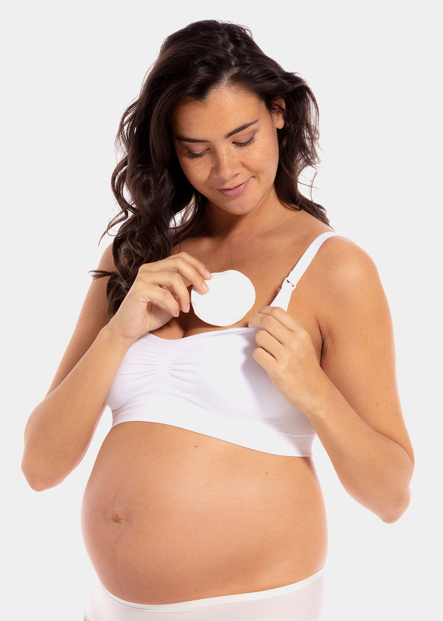 Front view of a model placing Nursing Pad in latte inside her bra. Round absorbent pad made of bamboo and cotton fibers, shown positioned within the bra cup for coverage.