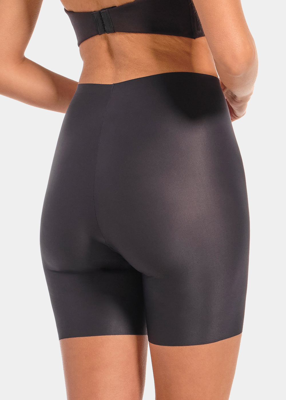 Back view of a model wearing Everyday Shaper Bermuda in black, mid-waisted seamless shapewear shorts. Long leg design extending to mid-thigh, with smooth fabric and seamless edges for invisible wear under clothing.