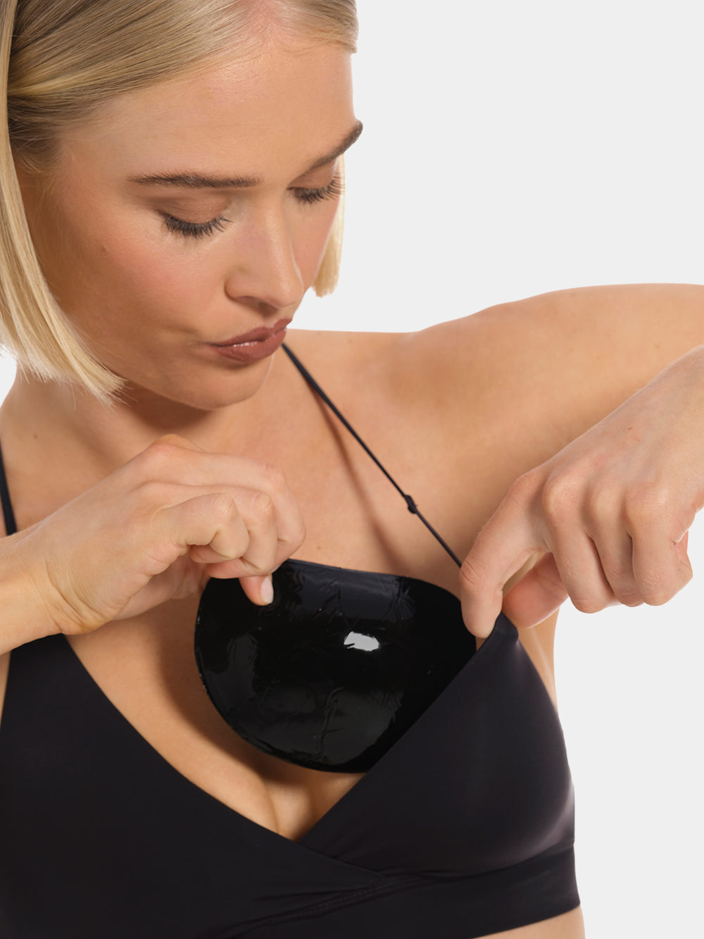Front view of a model holding Double Sticky Demi Push-Up Pads in black in front of her bra. Demi-shaped silicone bra inserts with smooth outer surface and curved shape visible before placement.