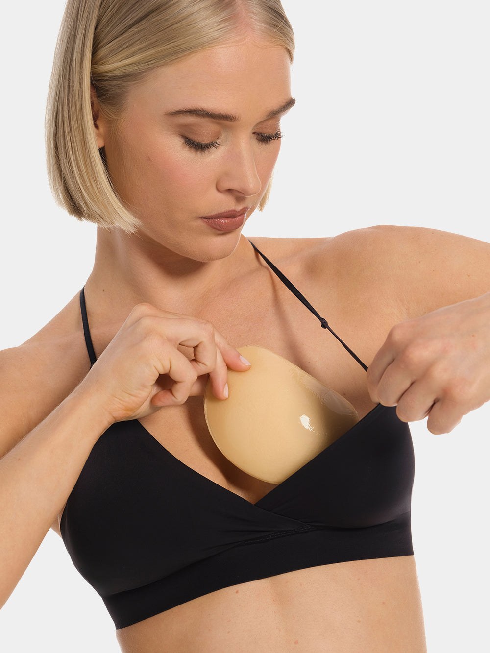 Front view of a model holding Double Sticky Demi Push-Up Pads in latte in front of her bra. Demi-shaped adhesive inserts shown before placement, with smooth outer surface and curved shape visible.