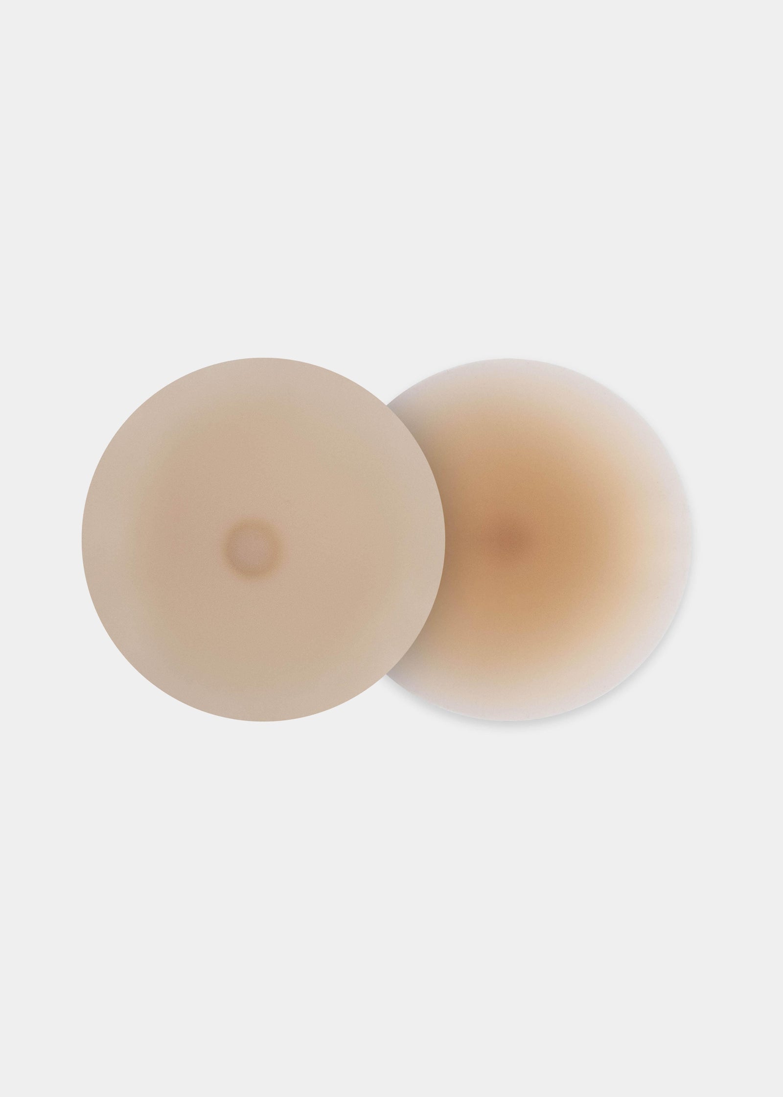Still product image of the latte-colored Show Your Nipples silicone nipple covers, displayed overlapping to show both the smooth outer surface and the inner skin-friendly adhesive layer.
