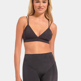 Woman wearing a dark gray sports bra and shorts set on a light gray background