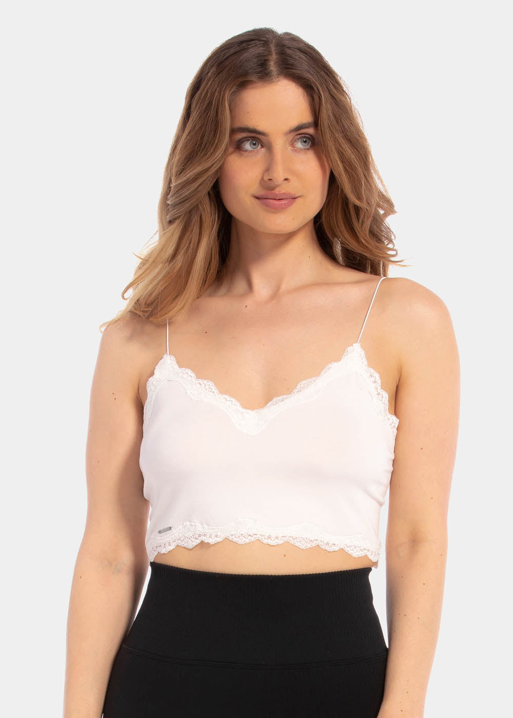 A woman wearing a white cozy crop top with V-neckline and lace detail, with ultra thin spaghetti straps.