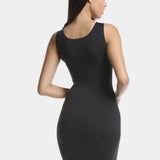 Back view of a model wearing Tone Your Body Dress in black, body-contouring tank dress. Smooth powerful recycled fabric providing firm shaping for back, hips, and legs, with seamless edges, smooth shoulders, and silicone-lined leg openings visible.