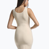 Back view of a model wearing Tone Your Body Dress in latte, body-contouring tank dress. Smooth powerful recycled fabric providing firm shaping for back, hips, and legs, with seamless edges, smooth shoulders, and silicone-lined leg openings visible.