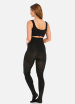 Back view of a model wearing Hi-Waist Slim Tights in black, 140 denier high-waist shaping tights. Smooth opaque fabric providing medium shaping for lower back, hips, and thighs, with silicone-trimmed waistband and reinforced toes visible.