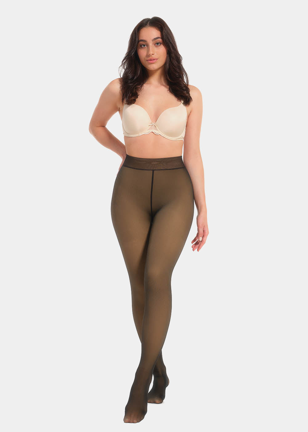 A model wearing high-waisted, fleece-lined brown tights with a sheer appearance. She is also wearing a white bra.