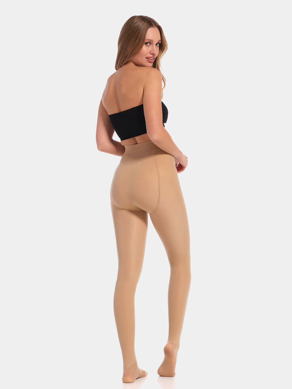 Back view of a model wearing MAGIC Tights in latte, high-waist warm fleece-lined tights. Smooth fabric providing medium shaping for lower back and waist, ladder-resistant finish, and sheer-look legs with unfleece foot section visible.