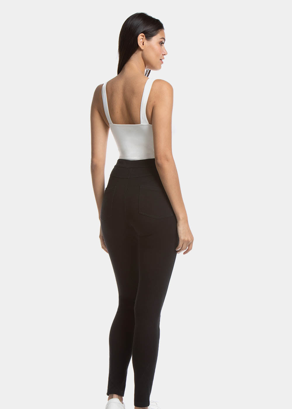 Back view of a model wearing Jegging in black, high-waist skinny-fit leggings with built-in shaping briefs. Soft stretchy fabric providing medium control for lower back and hips, lifted bottom zone, and functional back pockets visible.
