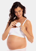 Front view of a model placing Nursing Pad in latte inside her bra. Round absorbent pad made of bamboo and cotton fibers, shown positioned within the bra cup for coverage.