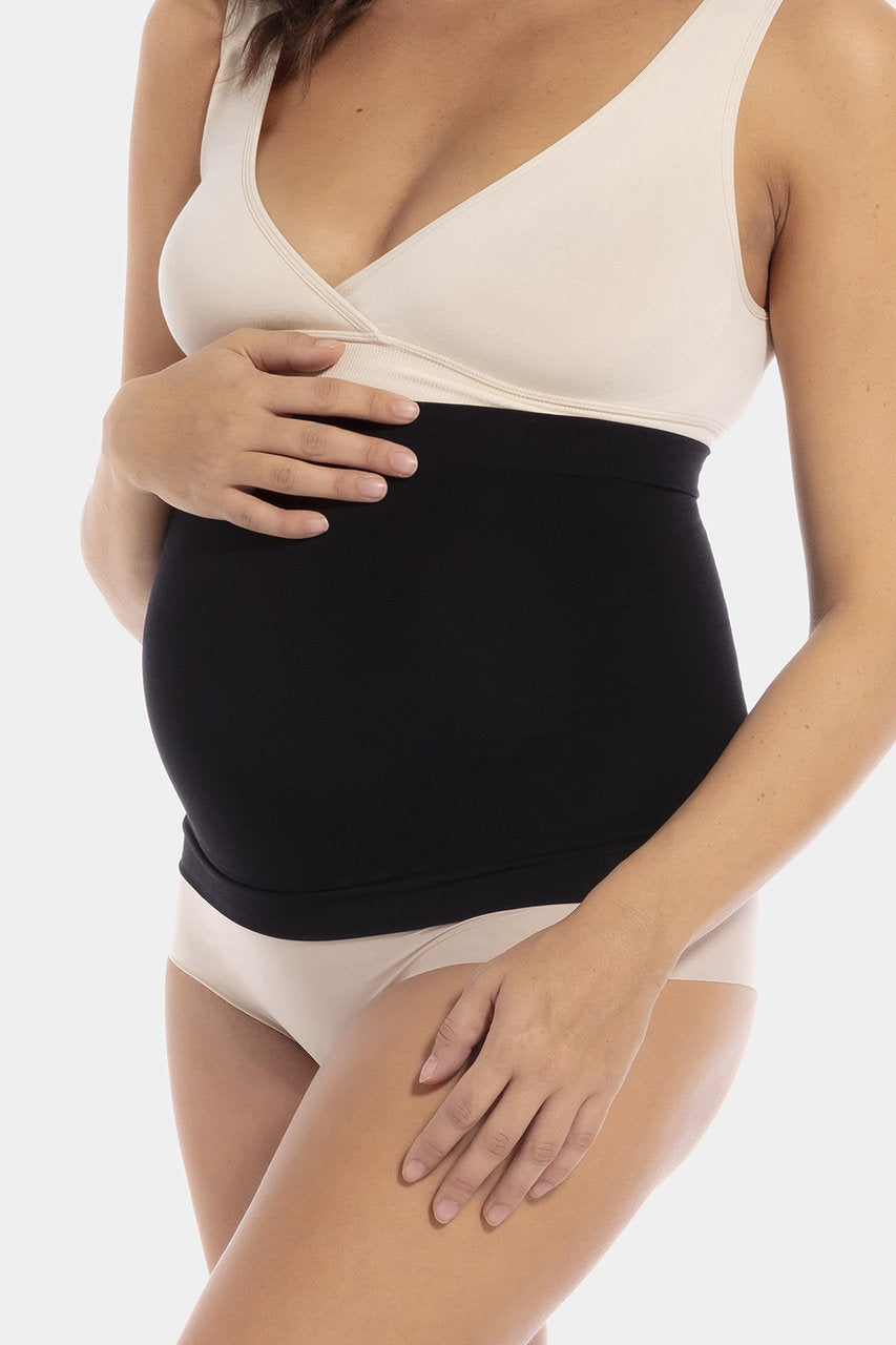 Front view close-up of a pregnant model wearing Mama Supporting Belly Band in black, seamless maternity band. Soft stretchable fabric with under-bump support panel and silicone trim at top and bottom visible, showing smooth fit over the belly.