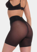 Back view cropped image of a model wearing Sheer & Sexy Shaping Short in black, mid-waist shaping shorts. Smooth fabric with sheer mesh panels and special lift zone at the buttocks visible, with seamless edges for invisible wear.