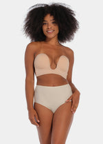 A woman wearing a cappuccino strapless, backless, and adhesive bra with a low U-plunge neckline.