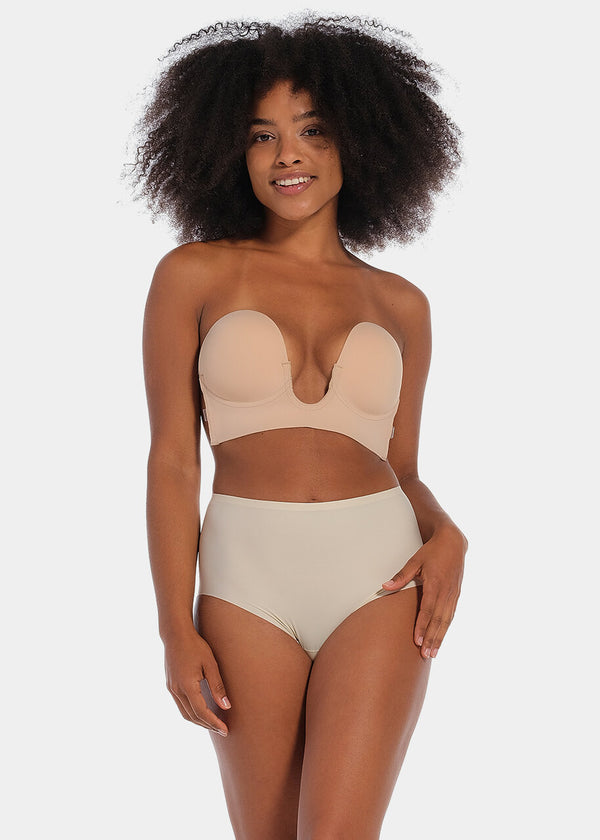 A woman wearing a cappuccino strapless, backless, and adhesive bra with a low U-plunge neckline.