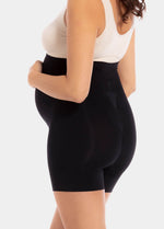 Back view of a model wearing Mama Supporting Short in black, over-the-bump seamless maternity shapewear shorts. Smooth stretchable fabric with mid-thigh length and seamless finish, showing supportive coverage over hips and upper legs.