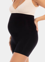 Side view cropped image of a model wearing Mama Supporting Short in black, over-the-bump seamless maternity shapewear shorts. Stretchable fabric covering belly and upper thigh, showing smooth finish and mid-thigh length.