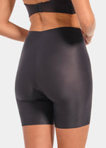 Back view of a model wearing Everyday Shaper Bermuda in black, mid-waisted seamless shapewear shorts. Long leg design extending to mid-thigh, with smooth fabric and seamless edges for invisible wear under clothing.