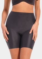 Front view of a model wearing Everyday Shaper Bermuda in black, mid-waisted seamless shapewear shorts. Cropped image showing waistband and upper thigh area, with smooth fabric and invisible finish under clothing.