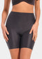 Front view of a model wearing Everyday Shaper Bermuda in black, mid-waisted seamless shapewear shorts. Cropped image showing waistband and upper thigh area, with smooth fabric and invisible finish under clothing.