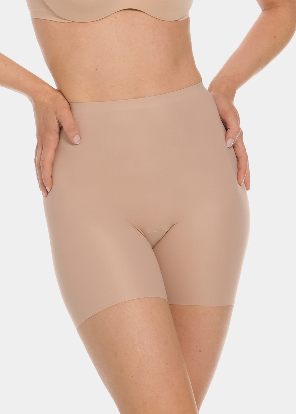Front view of a model wearing Everyday Shaper Bermuda in cappuccino, mid-waisted seamless shapewear shorts. Cropped image showing waistband and upper thigh area, with smooth fabric and long leg length for invisible shaping under clothing.