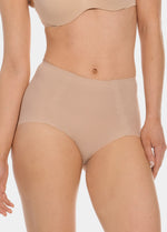 Front view of a model wearing Everyday Shaper Shorty in cappuccino, mid-waisted seamless shapewear shorts. Smooth fabric with short leg length, providing light shaping to lower tummy and back with invisible finish under clothing.
