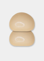 A beige-colored demi push-up pad with adhesive on both the inside and outside, designed for discreet lift and stay-put fit.