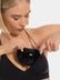 Front view of a model holding Double Sticky Demi Push-Up Pads in black in front of her bra. Demi-shaped silicone bra inserts with smooth outer surface and curved shape visible before placement.