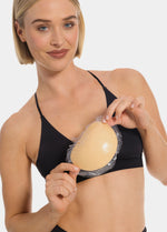 Front view of a model holding Double Sticky Demi Push-Up Pads in latte in her hands. Demi-shaped silicone bra inserts with smooth surface and curved shape, showing double-sided adhesive push-up design.