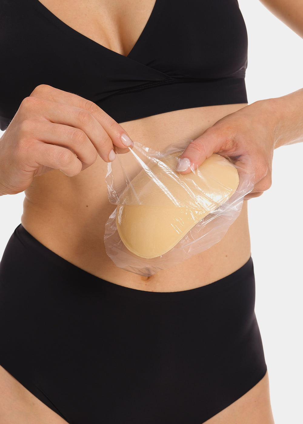 Person holding a breast push up pad in clear plastic wrap against a white background