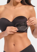 Front view of a model holding Sticky Push-Up Pads in black in front of her bra. Adhesive bra insert shown before placement, with smooth outer surface and curved shape visible.