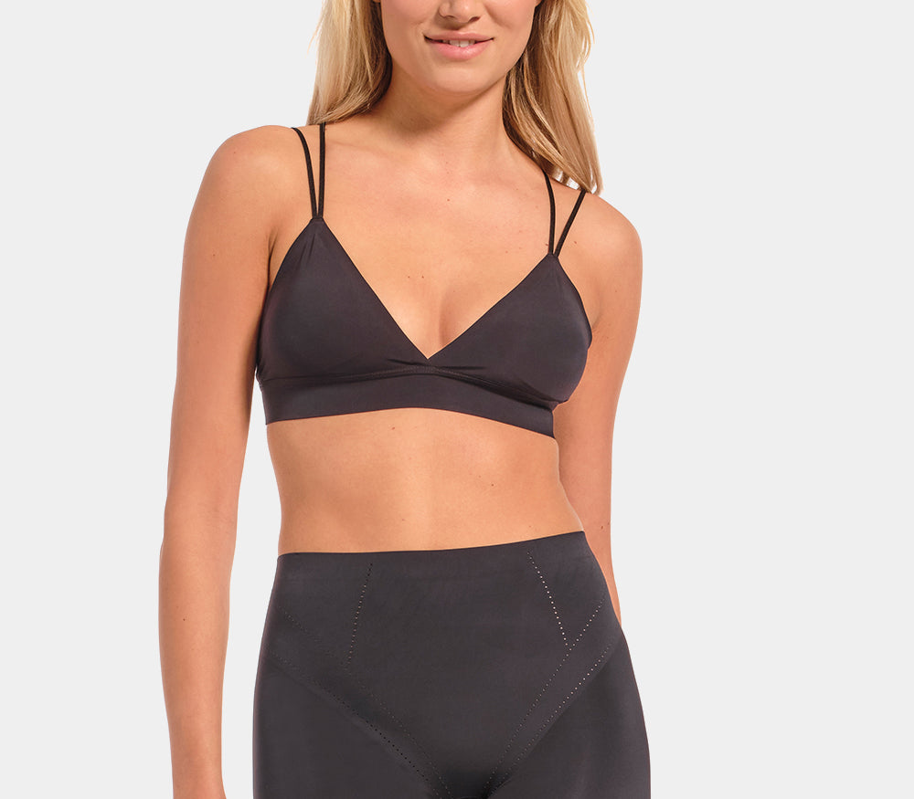 Woman wearing a dark gray sports bra and shorts set on a light gray background