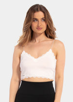 A woman wearing a white cozy crop top with V-neckline and lace detail, with ultra thin spaghetti straps.