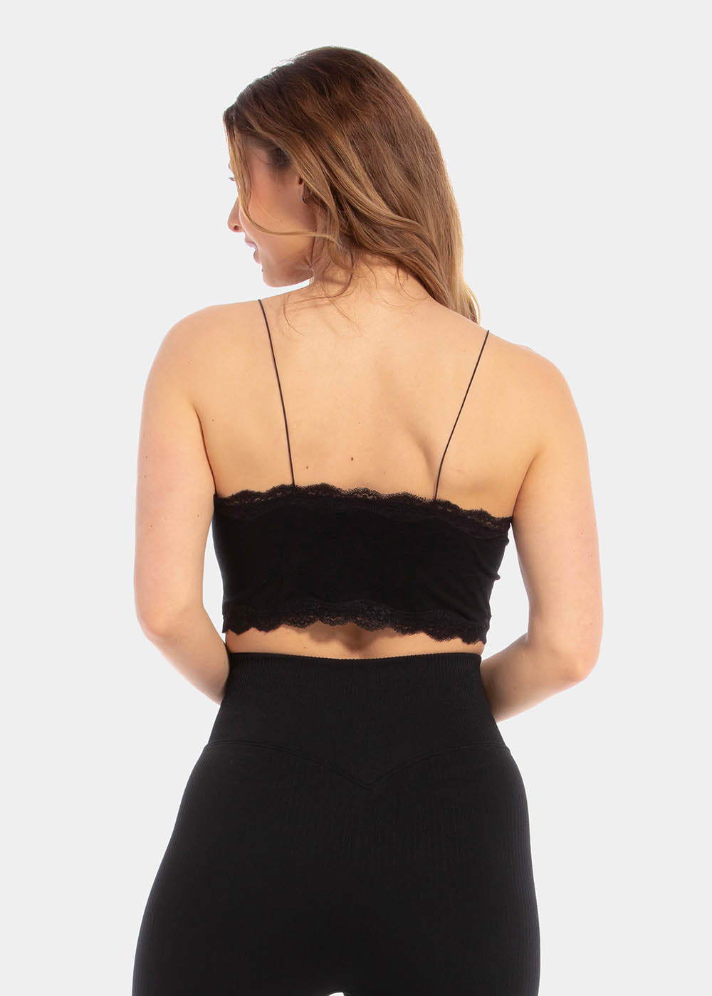 A woman wearing a black cozy crop top with V-neckline and lace detail, with ultra thin spaghetti straps. Shown from the back, seeing the lace and the thin spaghetti straps