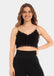 A woman wearing a black cozy crop top with V-neckline and lace detail, with ultra thin spaghetti straps.