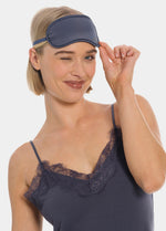 Woman wearing a navy sleep mask from MAGIC and lace-trimmed nightgown on a white background