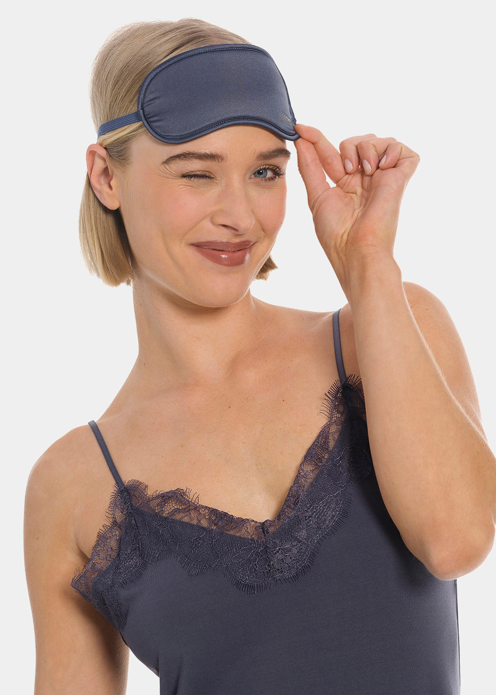 Woman wearing a navy sleep mask from MAGIC and lace-trimmed nightgown on a white background