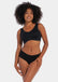 A woman wearing a black soft Sensual Soft Bra with removable inlay pads and wide straps, standing against a white background.